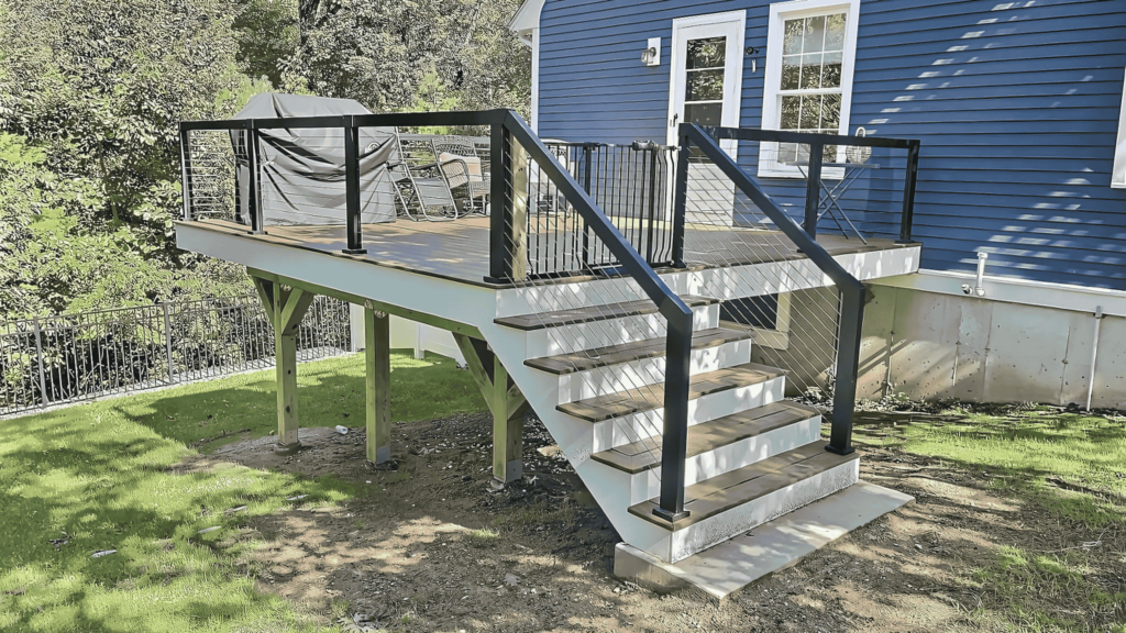 A newly built elevated deck with black metal railings attached to a blue house in Malden, MA.